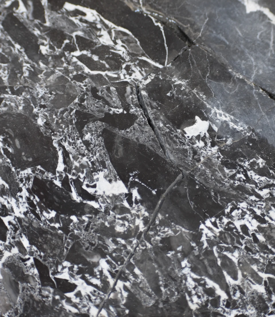 Detalle fotográfico de mármol oscuro brechado, con fragmentos negros y grises y vetas blancas.