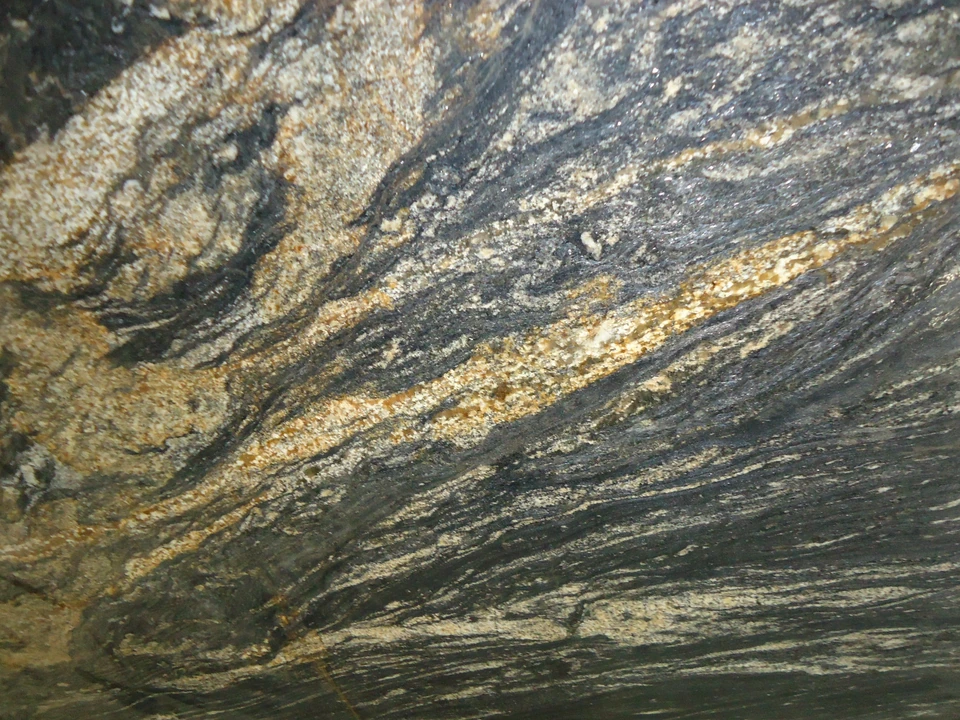 Fotografía de una losa de piedra natural con bandas oscuras, grises y doradas.