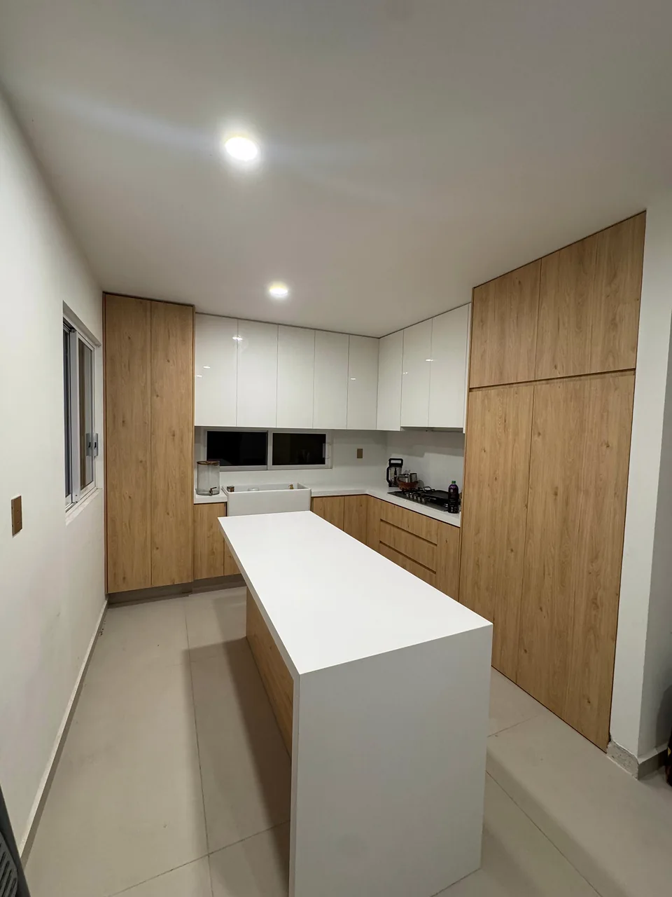 Cocina realizada por Infinity Design, con frentes de madera natural, alacenas claras e isla con cubierta blanca.