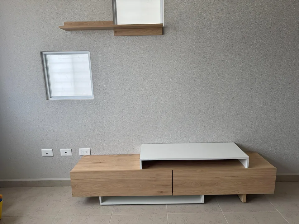 Mueble bajo para TV en tonos madera clara y blanco, con repisas sobre un muro gris.