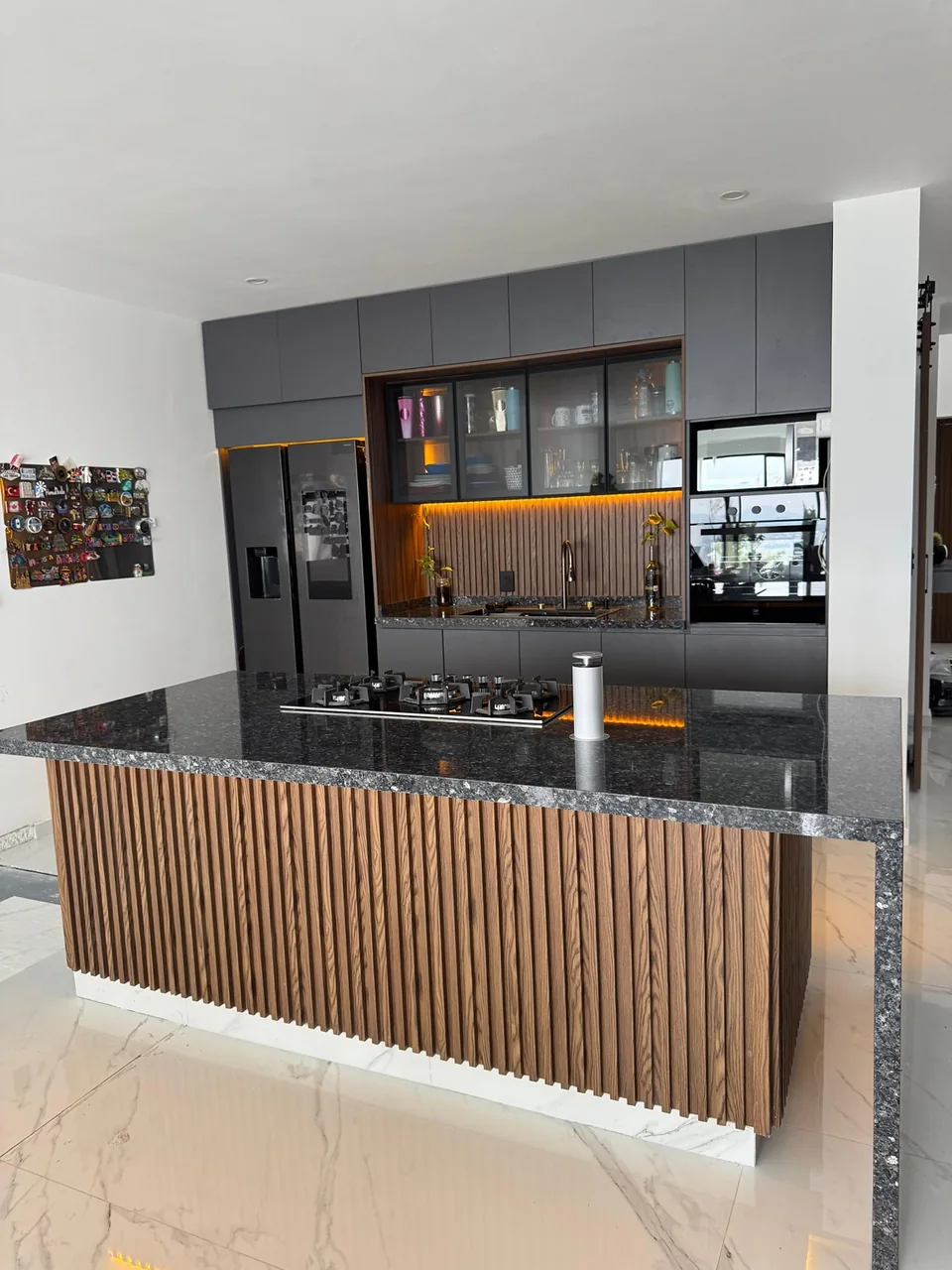 Cocina gris con vitrinas, iluminación cálida y una isla de frente panelado con cubierta oscura.