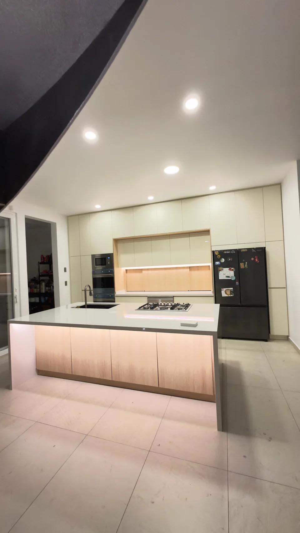 Cocina en tonos claros con almacenamiento de piso a techo e isla iluminada de frente en tono madera.