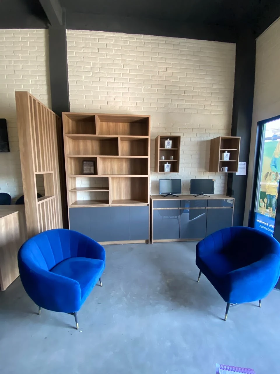 Mobiliario con repisas de madera, puertas grises y divisor de listones en un espacio de trabajo.