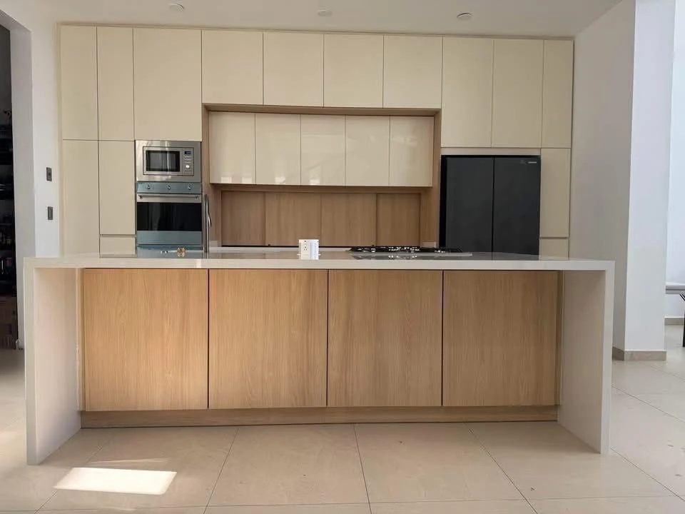 Cocina con alacenas claras, electrodomésticos integrados e isla en tono madera con cubierta clara.