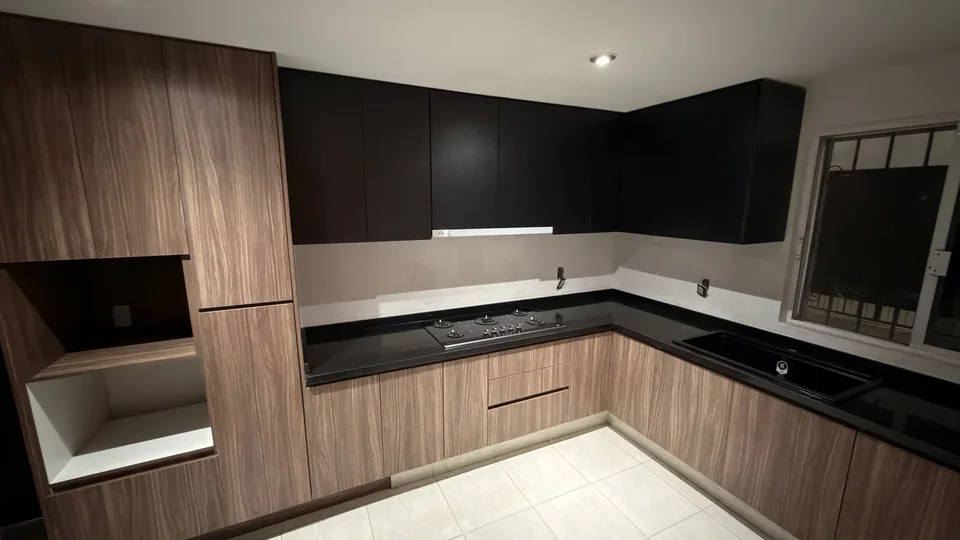 Cocina en L realizada por Infinity Design, con frentes en tonos madera y gabinetes negros.